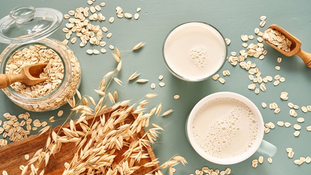 Glass of oat beverage with oats and oat stalks on a wooden table.